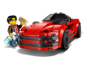 A LEGO minifigure in sunglasses polishes a red sports car with a sponge, holding a spray bottle. The car has black accents.