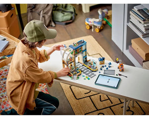 Child assembling LEGO City 60469 Central Train Station set on a table with a tablet.