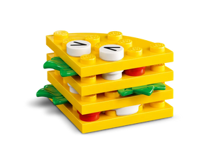 A layered LEGO food build featuring yellow plates, green leaf elements, red round bricks, and white round bricks with black markings.