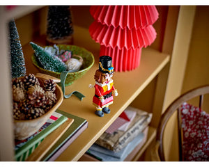 LEGO Nutcracker figure displayed on a wooden shelf alongside festive decorations like miniature trees and pinecones.