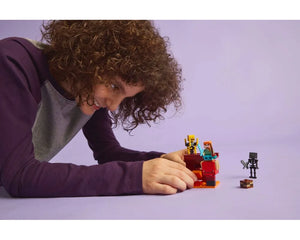 Person with curly hair smiles, playing with LEGO Minecraft 21266 The Nether Lava Battle set on a purple surface.
