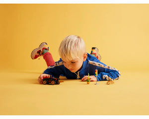 Blond boy on yellow floor playing with LEGO Super Heroes 10792 Drill Spinner Vehicle, minifigure, and traffic light.