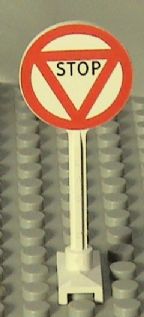 White LEGO road sign with a red circular outline and a red triangle pattern inside, featuring 'STOP' in black text.