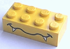 A yellow LEGO 2x4 brick with 8 studs, featuring a black wavy mouth and white fangs pattern on its side.