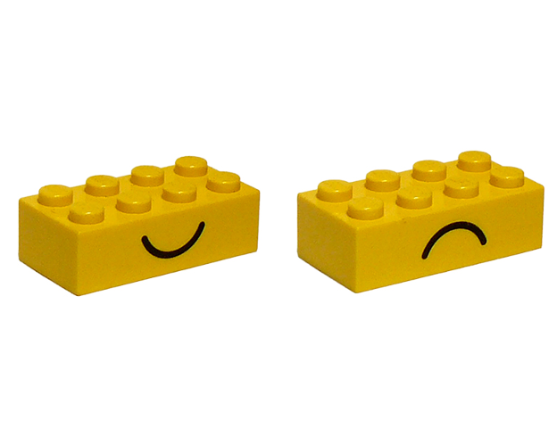 Two yellow LEGO 2x4 bricks, one with a black smile and the other with a black frown pattern.