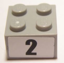 Grey LEGO 2x2 brick with four studs on top and a white sticker on the front showing a black number 2.