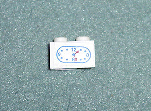 White LEGO 1x2 brick with a clock sticker pattern. Blue numbers 3, 6, 9, 12, and red hour and minute hands.