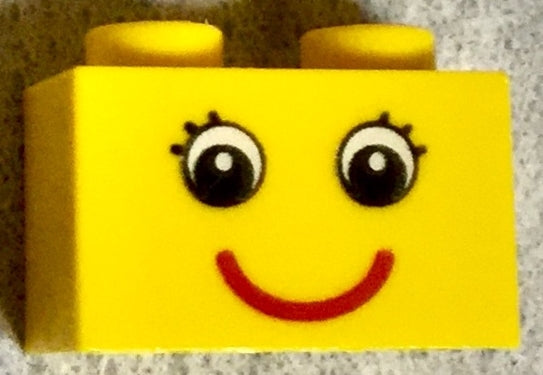 Yellow LEGO 1x2 brick with black eyes with eyelashes and a red smile pattern.