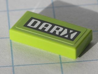 Lime green LEGO 1x2 tile with black and white 'DARX' pattern on a white grid surface.
