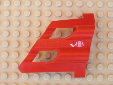 Red LEGO Technic Panel Fairing #1 Large Short, with large holes and a white 'V8' pattern, on a tan LEGO baseplate.