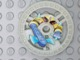 Light gray LEGO Technic 5x5 RoboRider Talisman Wheel disk featuring a yellow, brown, and blue robot pattern.