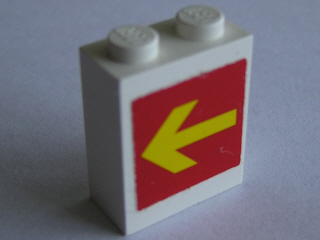 White LEGO 1x2x2 brick, part 3245bpb02, featuring a yellow arrow on a red background pointing left.