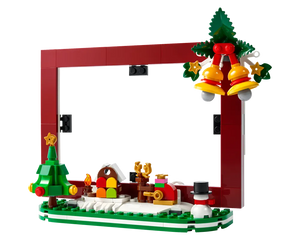 LEGO Christmas picture frame featuring a red frame, snowy base with a Christmas tree, colorful house, reindeer, snowman, and hanging bells.