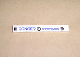 White LEGO 1x8 tile with a blue 'DANGER SHARP EDGES' sticker pattern, including exclamation mark and arrow symbols.