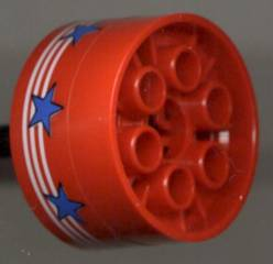 Red LEGO Technic wheel 20x30 with white stripes and blue stars pattern (sticker) on the side, showing six axle holes inside.