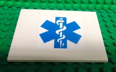 White LEGO Slope 10 6 x 8 with a blue Star of Life EMT sticker on a green studded background.