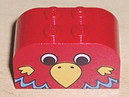 Red curved LEGO Duplo brick with four studs on top, featuring a yellow, brown, and blue parrot head pattern on the front.