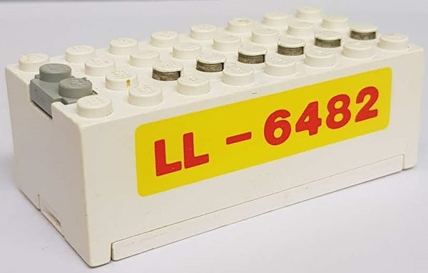 White LEGO 4760c01pb03 Electric 9V Battery Box Small, red 'LL-6482' on yellow sticker, gray studs, metal contacts.