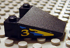 Black LEGO 4x4 wedge taper piece with a yellow and blue splash pattern and a number '3' on the side, on a studded baseplate.