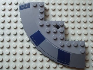 Grey LEGO 10x10 round corner brick with sloped edge, axle hole, and dark blue rectangles pattern, on a white baseplate.