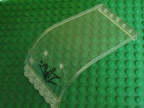 Clear LEGO 2572pb04 curved panel 6x6x9 with graffiti and bullet hole pattern on a green baseplate.