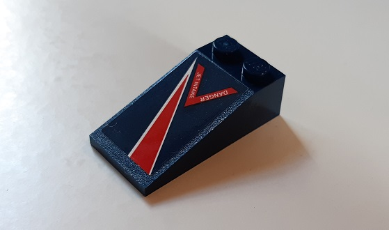Dark blue LEGO 4x2 slope brick with red and white 'DANGER JET INTAKE' sticker, angled view.