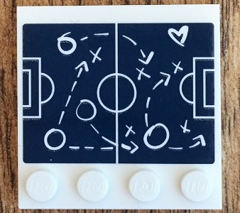 White LEGO 4x4 tile with dark blue soccer field diagram sticker, showing white tactical plays with arrows, circles, crosses, a '6' and a heart.