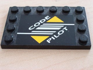 Black LEGO 4x6 modified tile with studs on edges, featuring a white and yellow Code Pilot sticker.