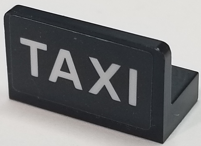 Black LEGO Panel 1 x 2 x 1 with white 'TAXI' text on the front, typical of a taxi roof sign.