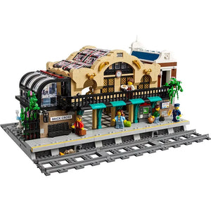 LEGO BrickLink Brick Cross train station set: tan building, glass roof, platform with minifigures, and train tracks.