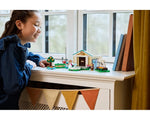 Girl admiring LEGO Animal Crossing 77056 Blathers's Museum Collection set on a white dresser by a window.
