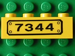A yellow LEGO 1x4 brick with a black rectangular pattern and the number '7344' printed in black. It rests on a green LEGO surface.