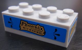 White LEGO 2x4 brick with a blue sticker featuring 'Phoenix Club' in a golden banner on its side.