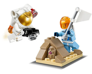 Two LEGO astronauts: one in white taking a photo, one in blue planting a flag next to a rock with a purple crystal.