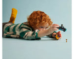 Red-haired child plays on a blue floor with two LEGO go-karts: one black and teal, one yellow and red, and a trophy.