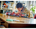 A boy playing with a LEGO City 60423 Downtown Streetcar set, placing a minifigure onto the red train and station.