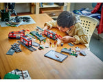 A child plays with LEGO City 60423 Downtown Streetcar set, featuring red trams, tracks, and a station on a wooden table.