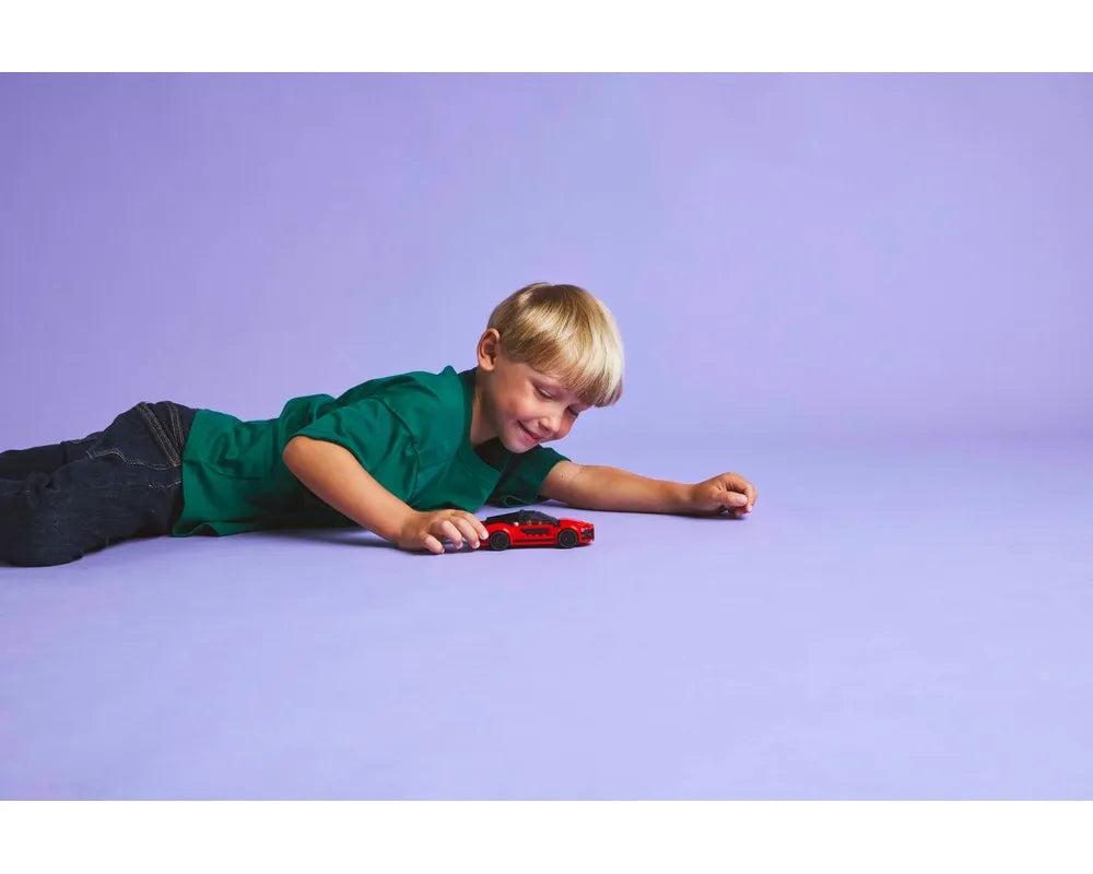 Boy lying on purple floor playing with red LEGO City 60448 Sports Car.