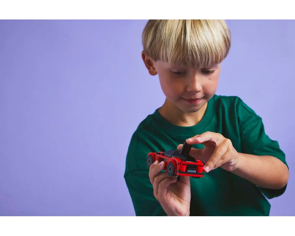 A child in a green shirt holds a red LEGO City 60448 Sports Car, interacting with its features.