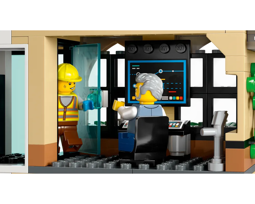 Two LEGO minifigures in a train station: a construction worker entering an office, and an older man at a desk with a monitor.