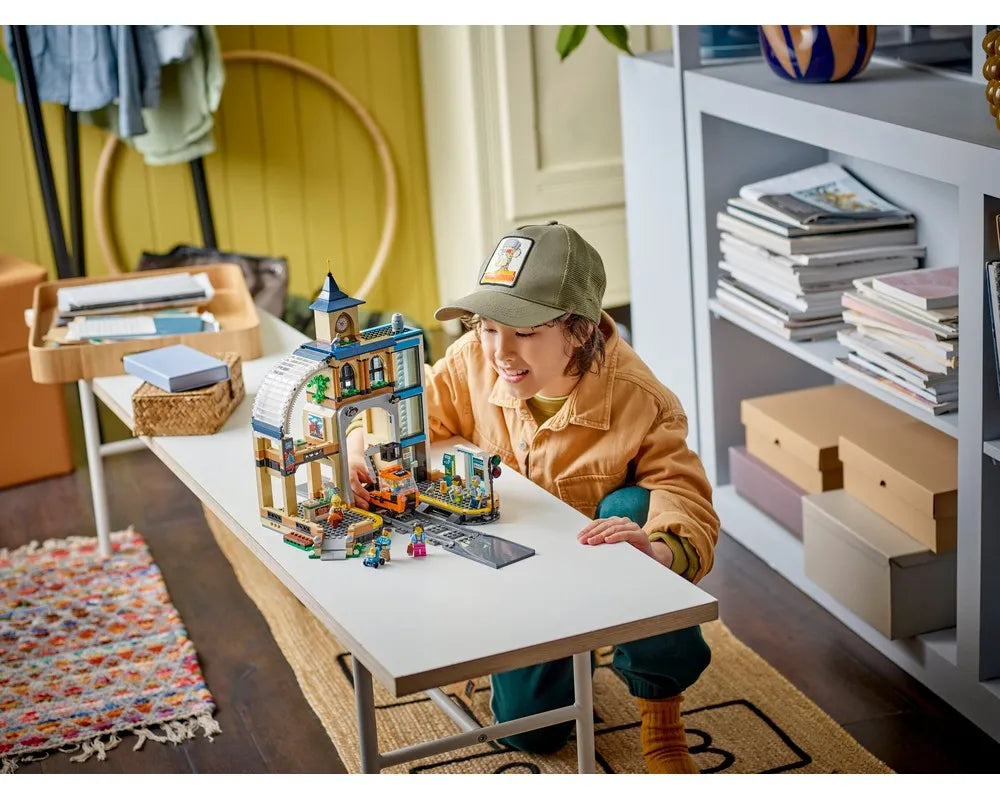 A child plays with the LEGO City 60469 Central Train Station set, featuring a building, forklift, and minifigures.