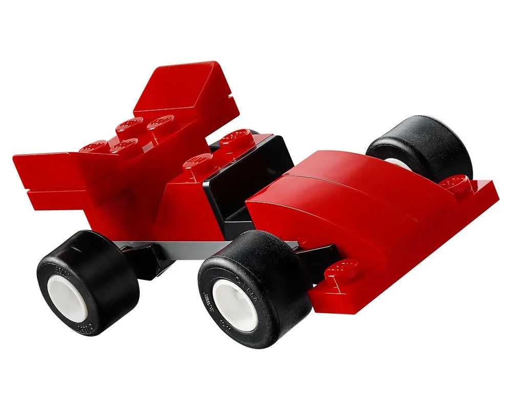 Red LEGO car model made from basic building bricks and black wheels with white hubs, on a white background.