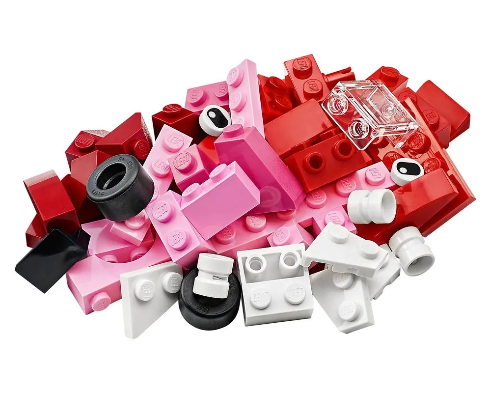 Pile of red, pink, white, and black LEGO bricks and elements, including eyes, tires, and a clear brick.