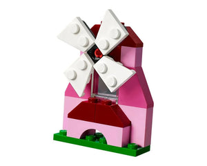 A small LEGO windmill, built from pink and dark red bricks, with four white rotating blades, standing on a green baseplate.
