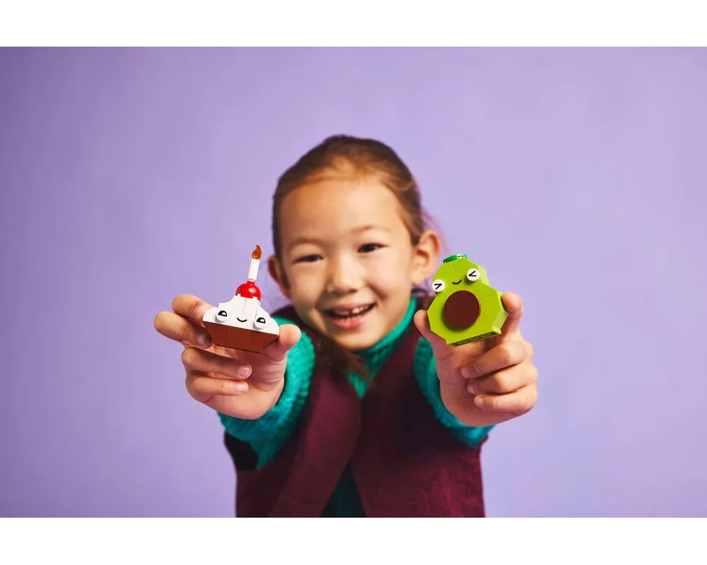 Smiling child holds LEGO cupcake with candle and green avocado from Creative Food Friends set 11039.