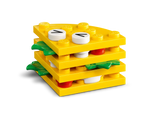 A layered LEGO food build featuring yellow plates, green leaf elements, red round bricks, and white round bricks with black markings.