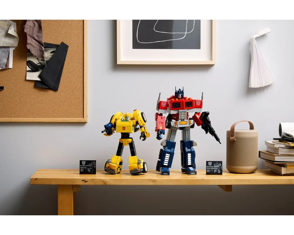 LEGO Bumblebee (yellow) and Optimus Prime (red/blue) Transformer figures on a wooden shelf with display plaques.