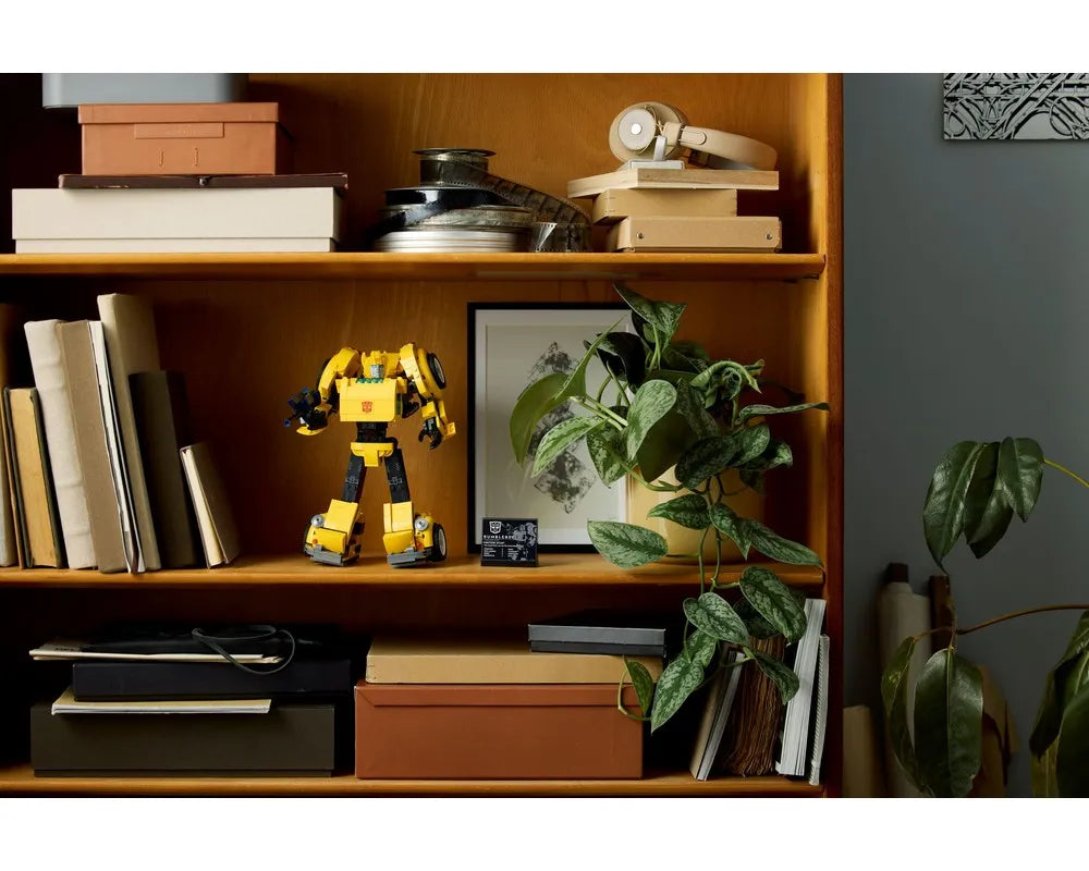 Yellow LEGO Creator 10338 Bumblebee figure displayed on a wooden shelf with books and a potted plant.