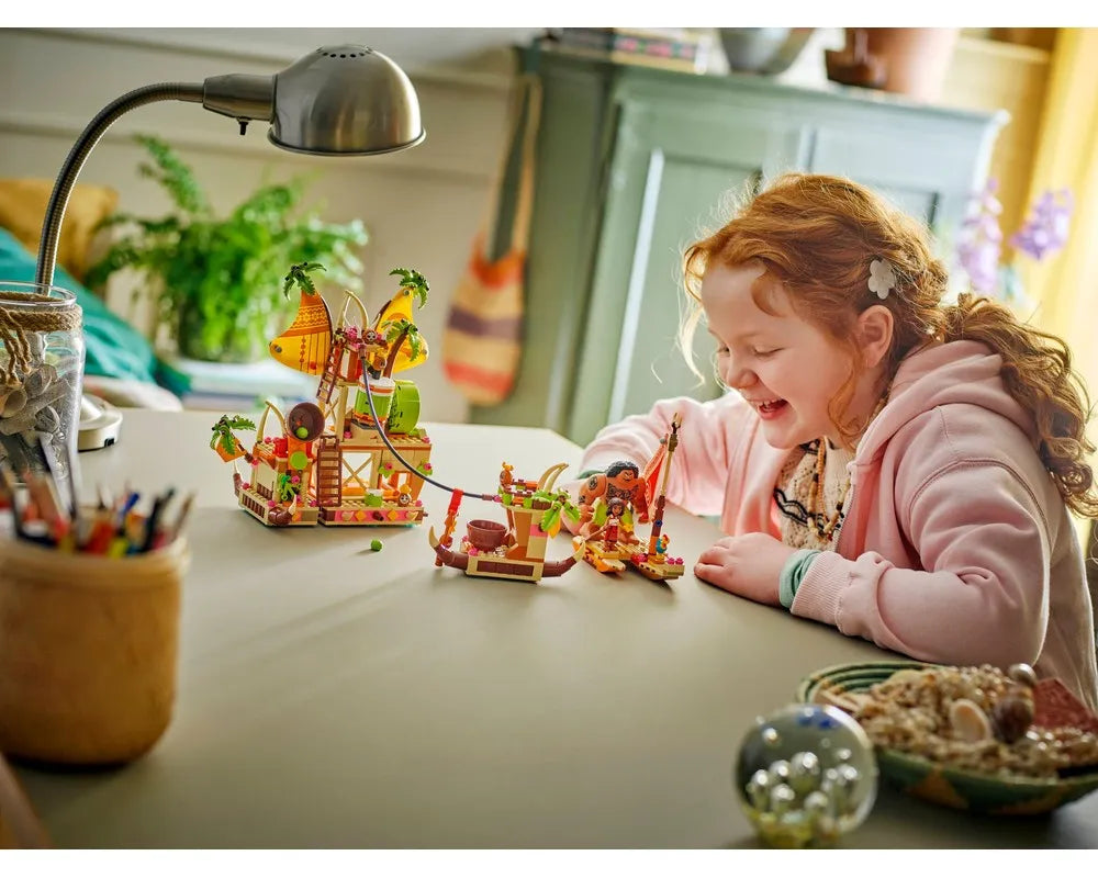 A smiling girl plays with the LEGO Disney 43258 Kakamora Barge set, featuring a tropical island-like structure and a small boat.