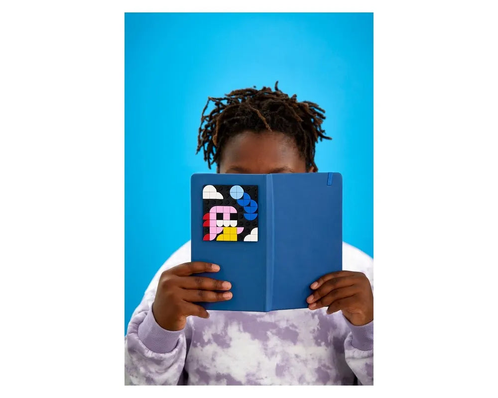 Person holding a blue notebook featuring a LEGO Dots 41954 adhesive patch with colorful abstract design.